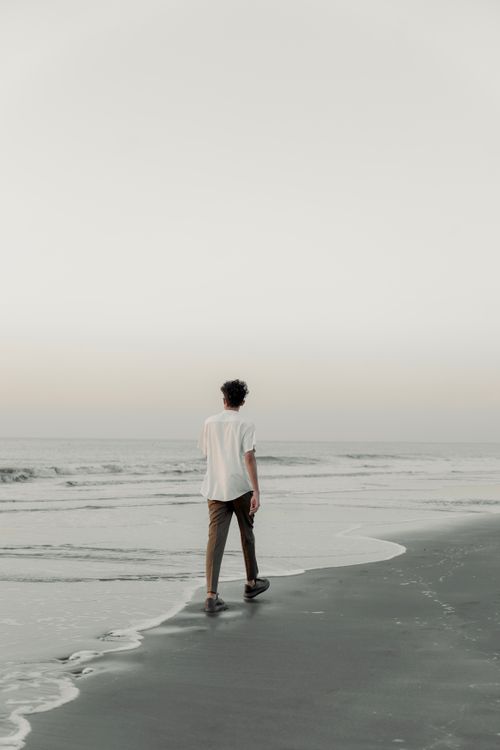 Free Man walking along a serene beach during sunset, capturing the essence of tranquility and solitude. Stock Photo