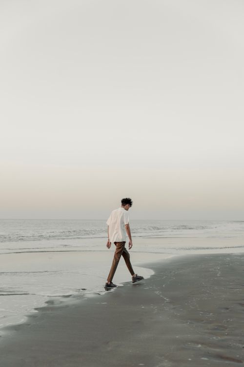 Free A man walks along a serene beach at sunset, exuding solitude and peace. Stock Photo