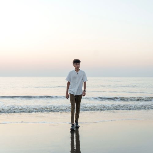 Free A man walks along the beach in a white shirt as the sun rises over the calm sea. Stock Photo