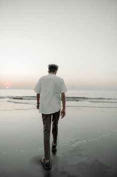 Back view of a man walking on a tranquil beach during sunset. Ideal for themes of relaxation and solitude.