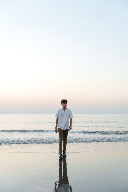 Free A fashionable man in a white shirt walks along a peaceful seashore at twilight. Stock Photo