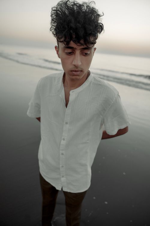 Free Portrait of a young man standing on a tranquil beach at dusk. Stock Photo