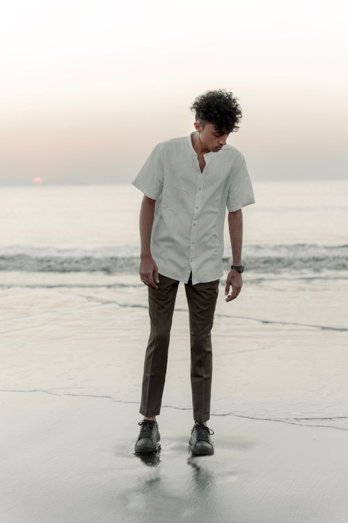 Free Stylish man in a white shirt and brown pants standing by the shore at sunset. Stock Photo