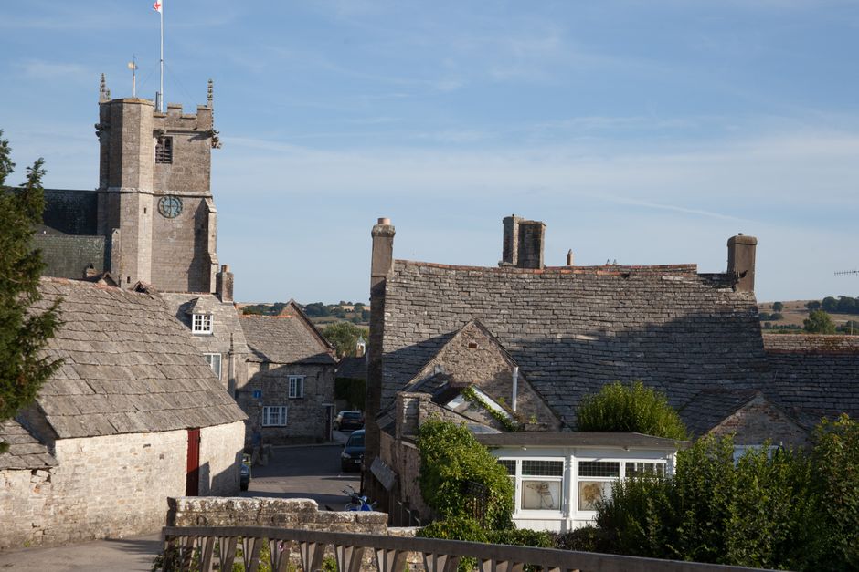 Charming view of historic rooftops and tower in Corfe Castle village, England.
