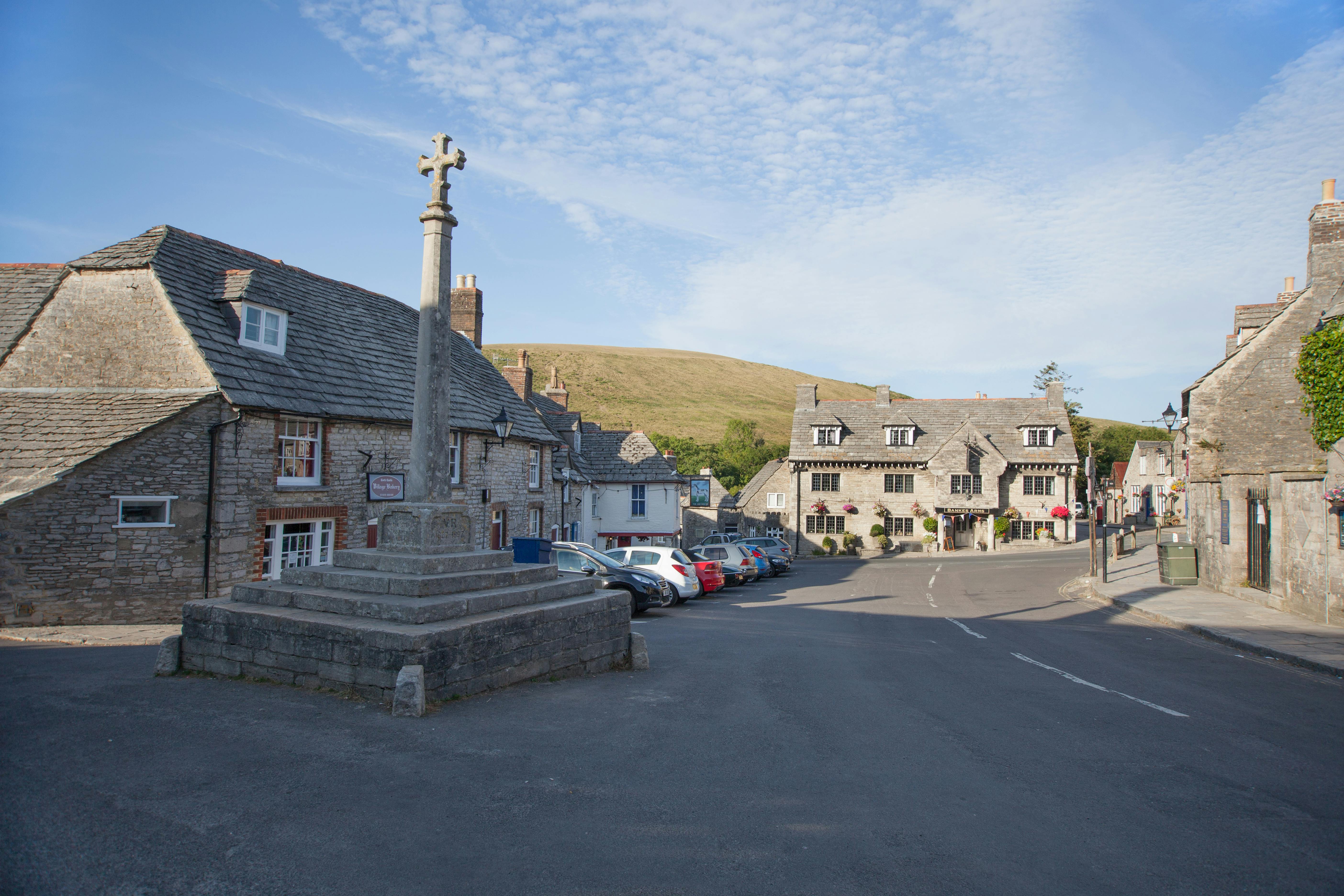Picturesque street view in Corfe Castle, England, showcasing stone buildings and a historical monument.