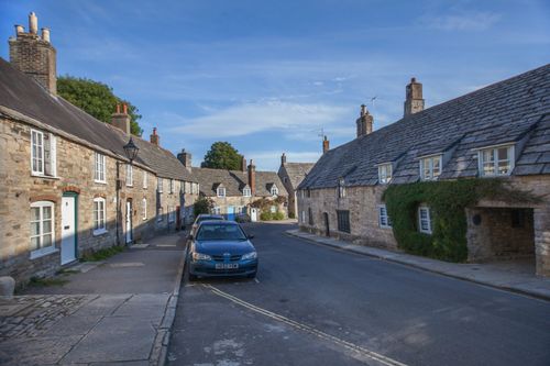 Free Quaint stone cottages line a picturesque street in Corfe, Dorset, England, under a clear blue sky. Stock Photo