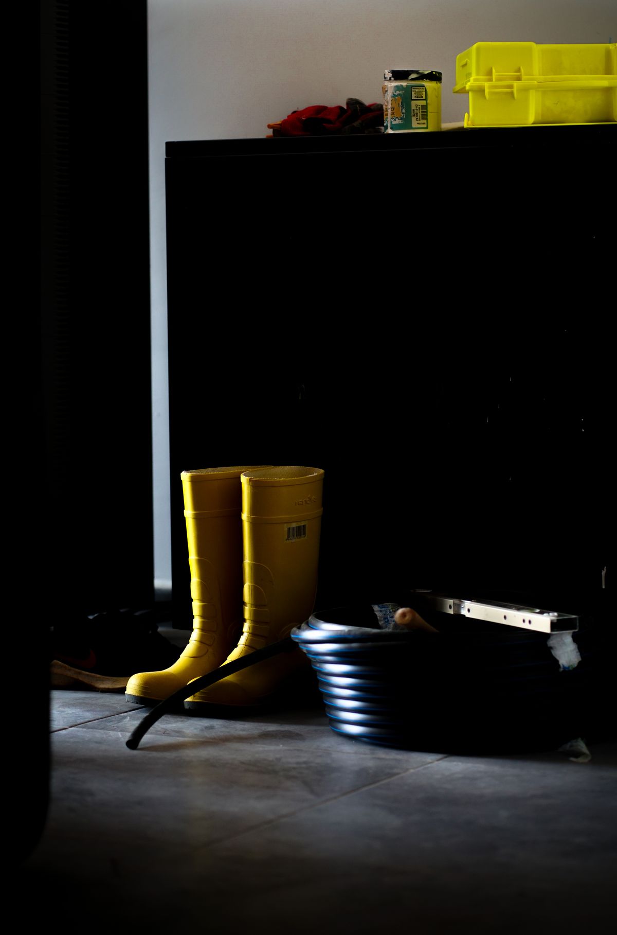 Yellow rain boots standing indoors in a moody drying corner after wet weather