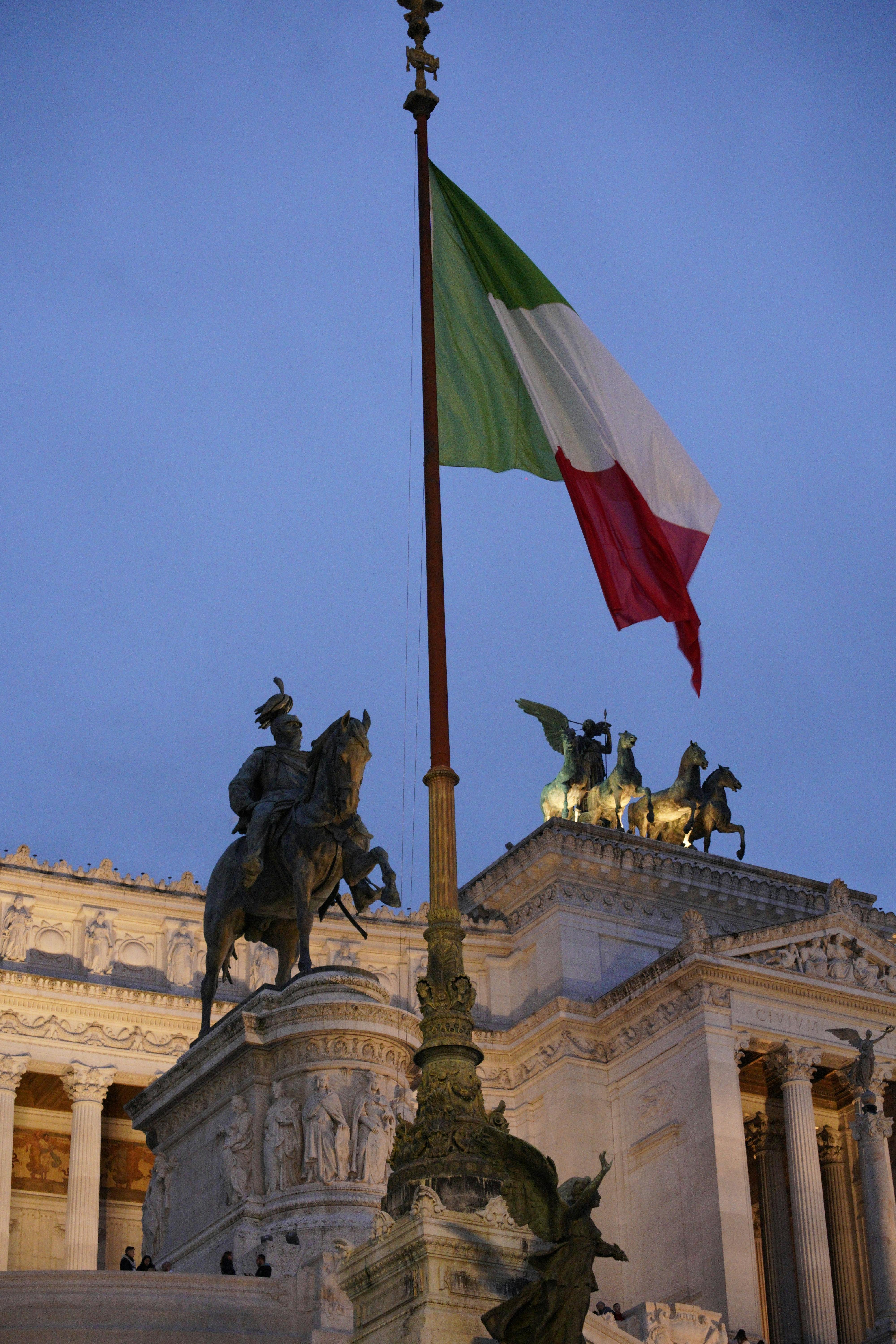 Low angle view of the Vittorio Emmanuele II monument in Rome with the Italian flag at dusk.