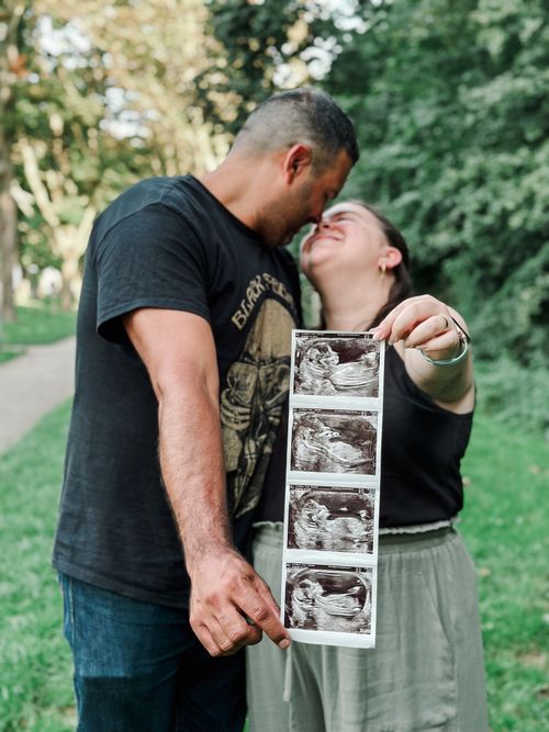 Free Happy couple holding ultrasound pictures, celebrating pregnancy in a sunny park. Stock Photo