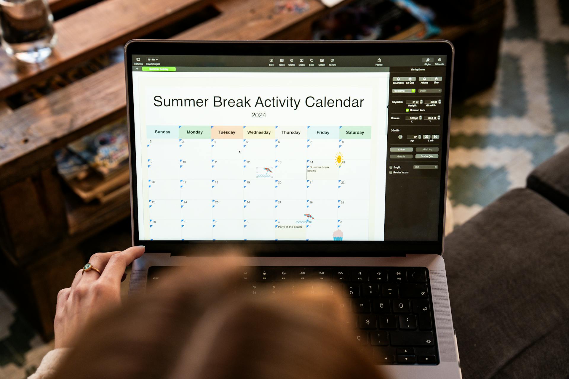 A woman uses a laptop to organize a 2024 summer break activity calendar from home.