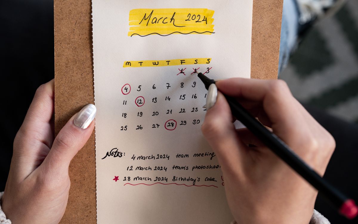 Close-up of a woman's hands organizing a planner for March 2024 with handwritten notes and highlights.