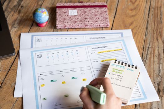 Person planning tasks with a calendar and notepad on a wooden table.