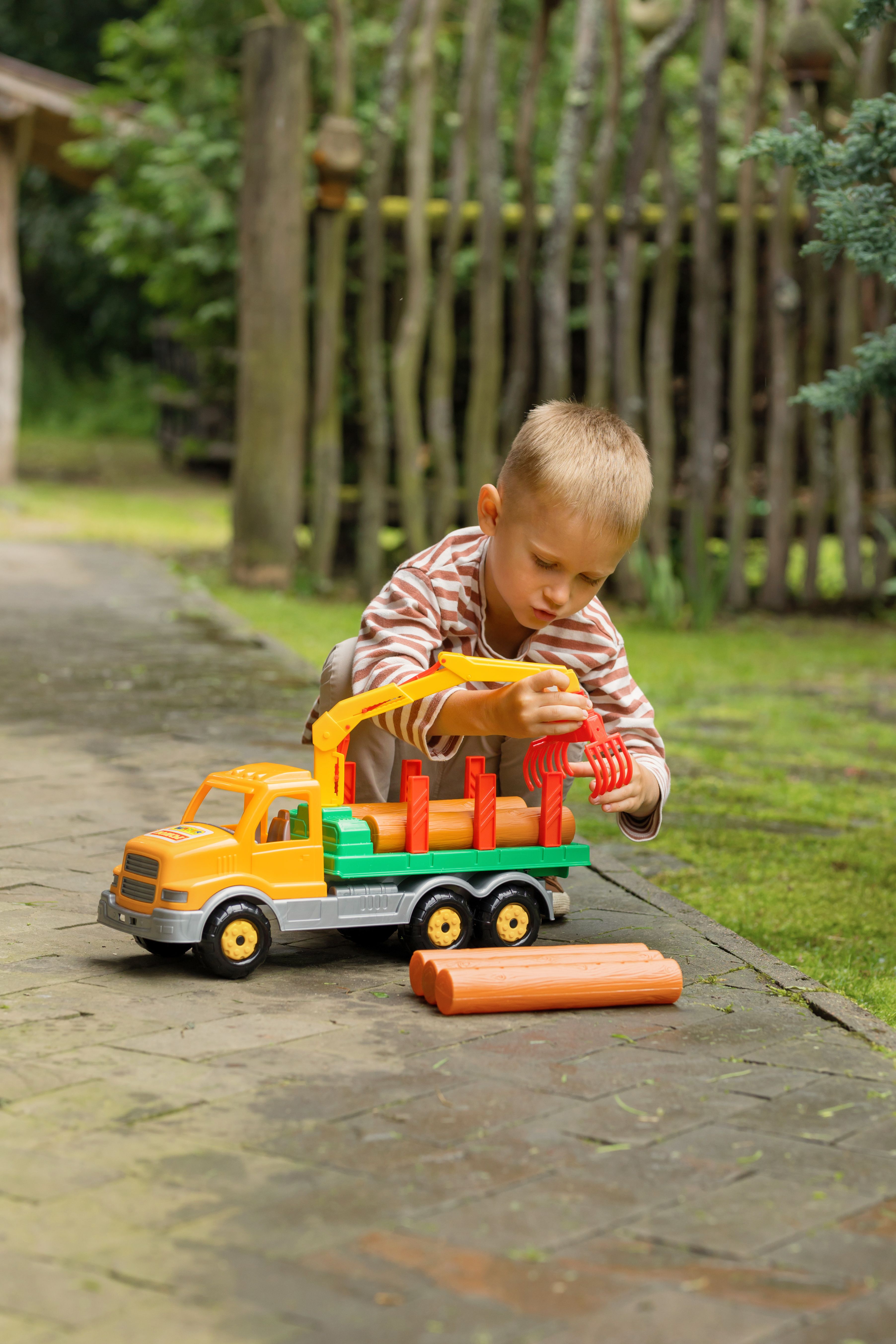 A young boy intently plays with a colorful toy truck on a stone pavement outdoors.