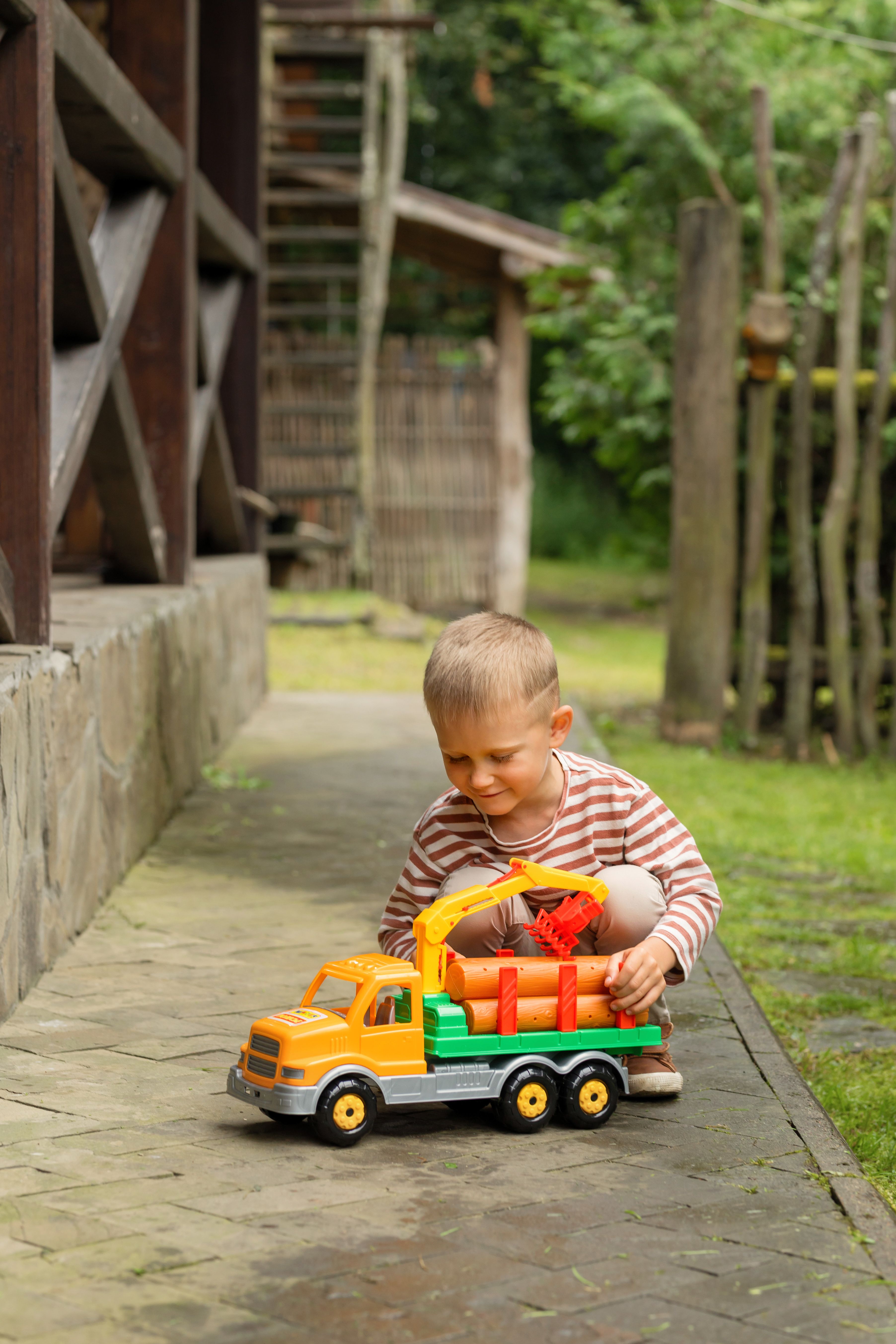 A young boy enjoys playtime with a colorful toy truck in a garden setting during summer.