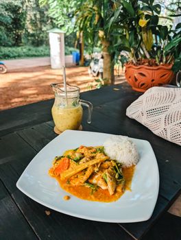 Enjoy a flavorful Thai curry with rice, served outdoors with a refreshing beverage.