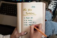 A person writes 2024 New Year's resolutions in a notebook. Concept of planning and personal goals.