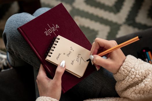 Woman writing future plans in a 2024 planner with focus on personal goals and organization.