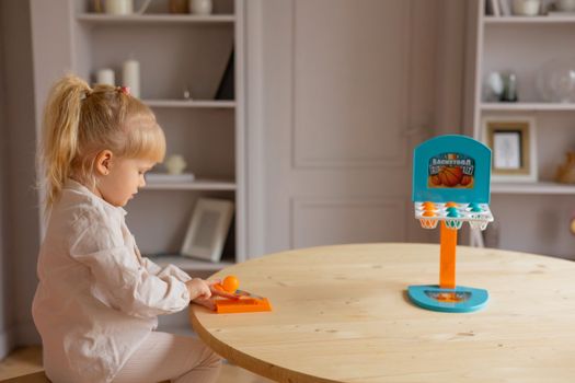 Young girl enjoying a fun indoor activity with a mini basketball hoop toy on a table.