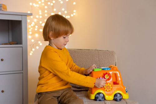 Free A young child enjoys playing with a colorful toy truck indoors, surrounded by warm lights. Stock Photo