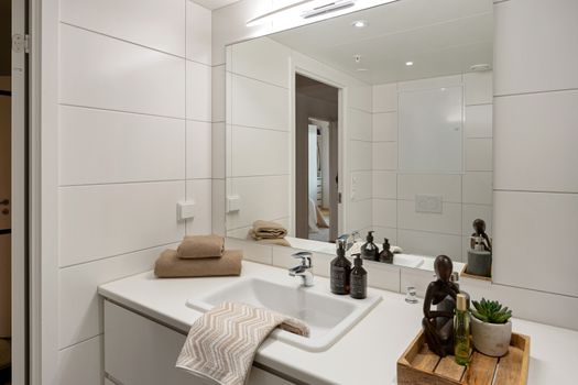 Elegant modern bathroom with white tiles, large mirror, and stylish accessories like towels and toiletries enhancing the decor.