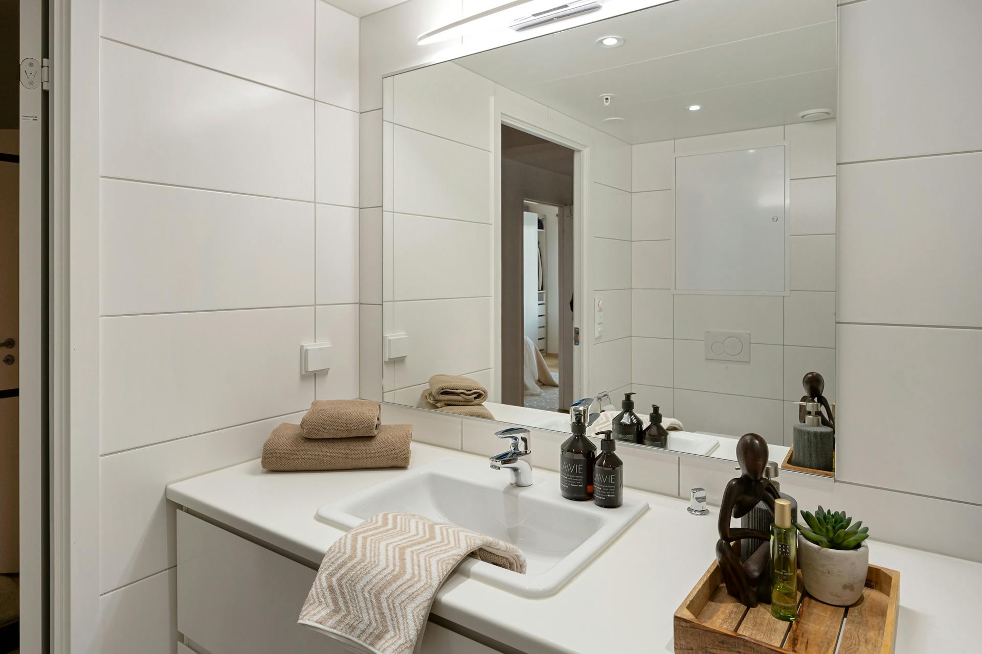 Elegant modern bathroom with white tiles, large mirror, and stylish accessories like towels and toiletries enhancing the decor.
