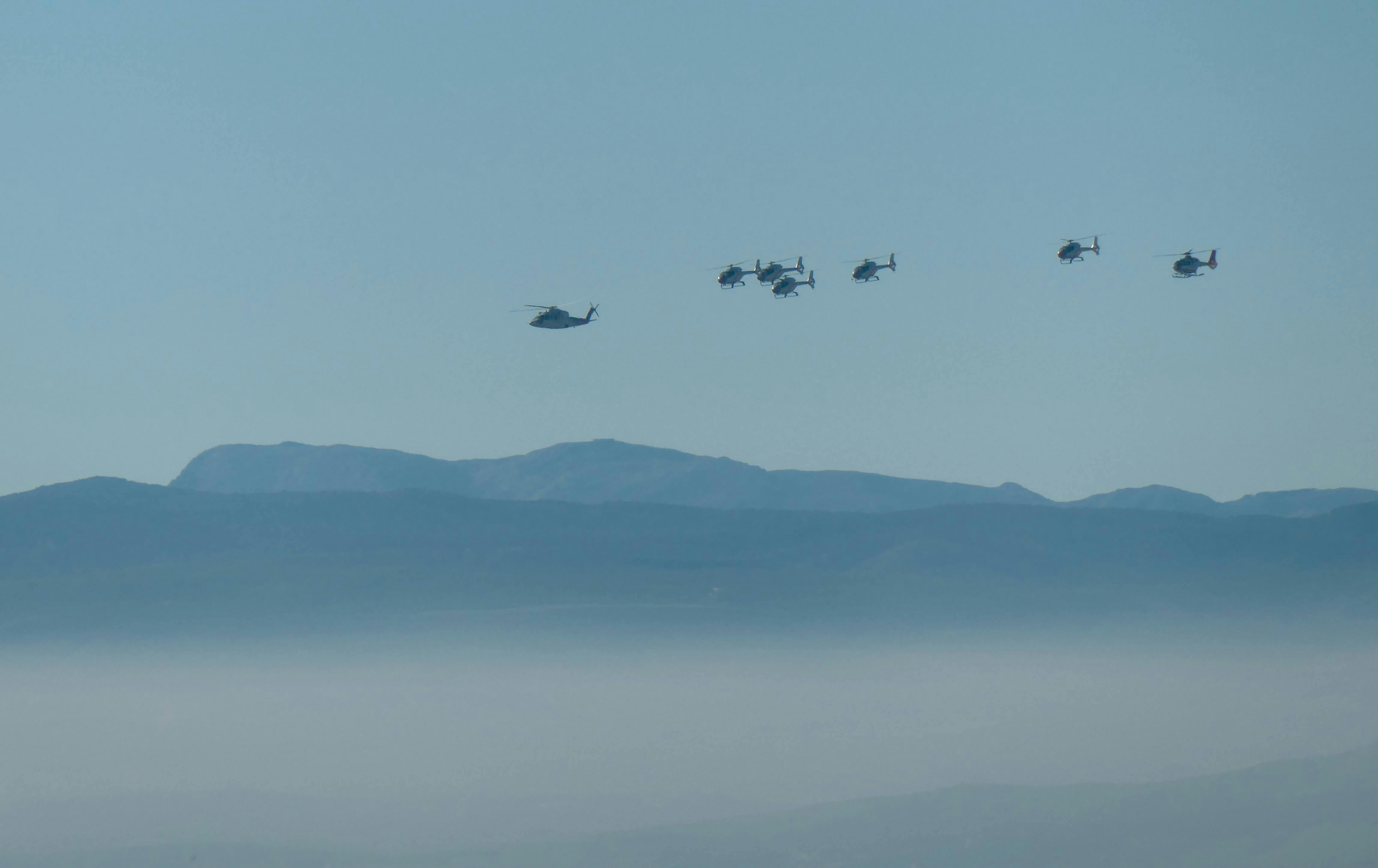 Aerial view of helicopters flying in formation over misty mountains against a clear sky.