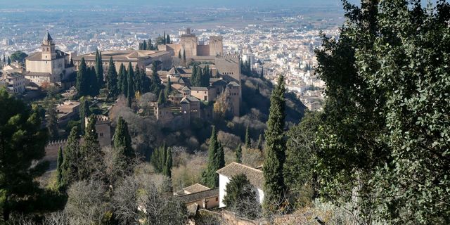 Stunning view of the Alhambra with Granada cityscape in Spain, surrounded by lush cypress trees.
