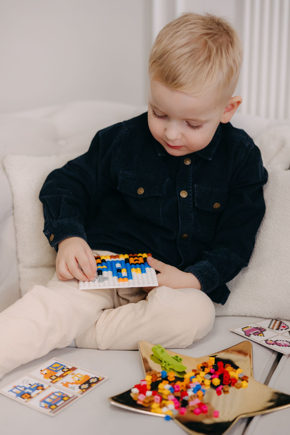 A young child engaged in creative play with building blocks and minifigures kept in small tins