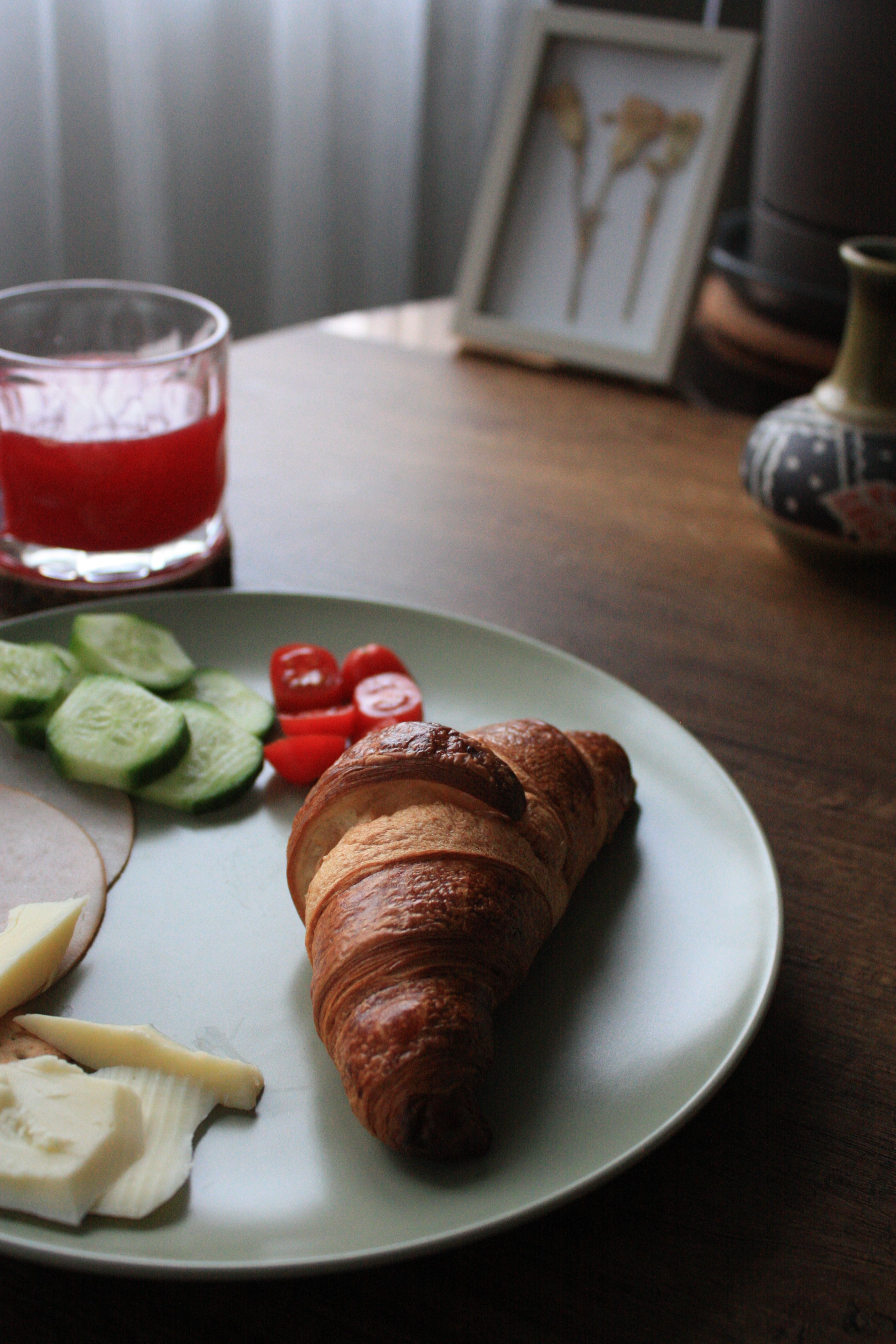 A cozy breakfast scene featuring a croissant, sliced vegetables, and a refreshing drink.