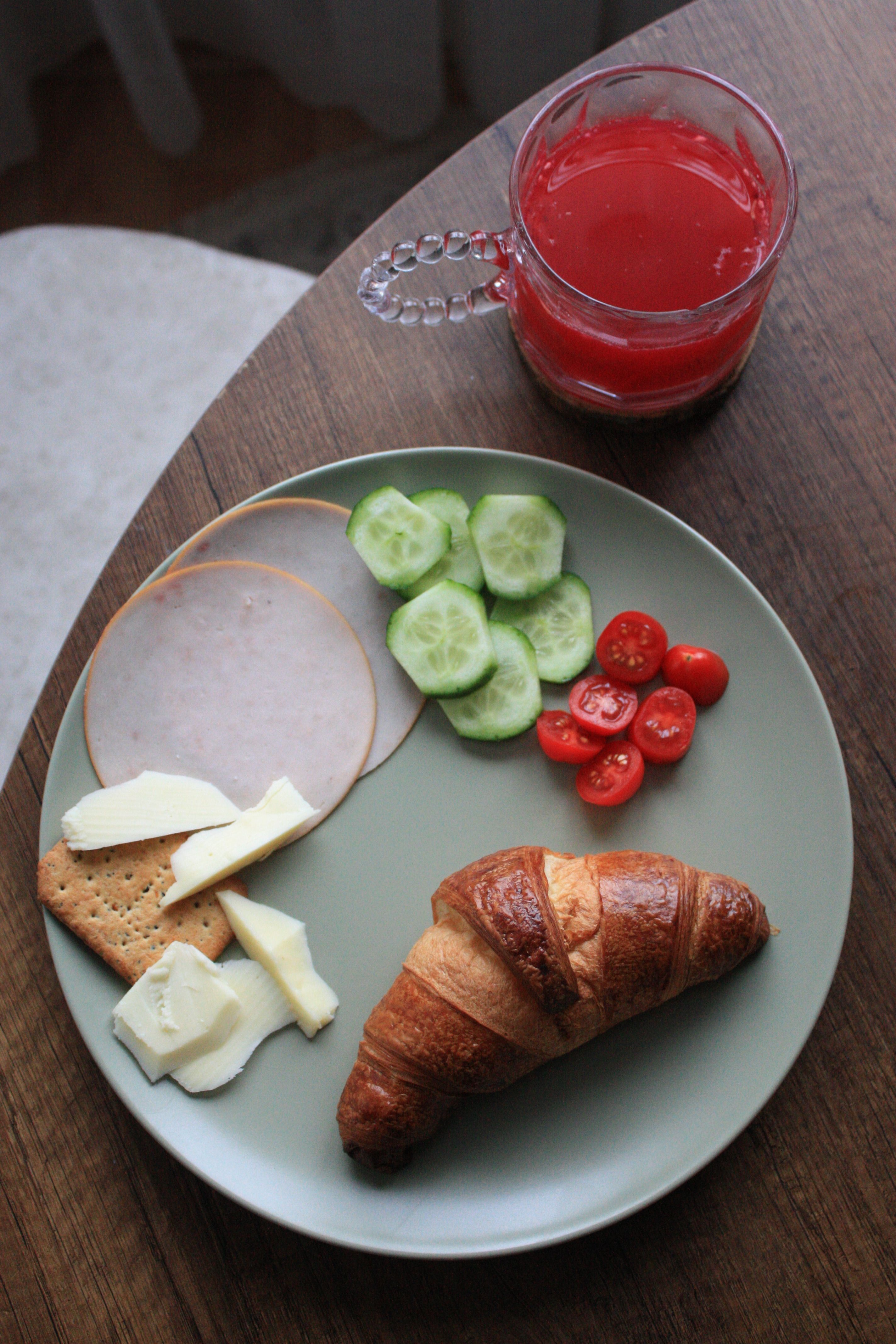A tasty breakfast spread featuring a croissant, veggies, cheese, and fresh juice.