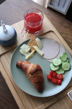 A healthy breakfast spread featuring croissant, cheese, ham, vegetables, and a refreshing drink.