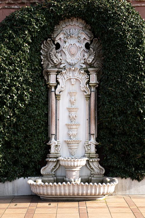 Free Elegant stone fountain with intricate designs set against lush ivy outdoors. Stock Photo