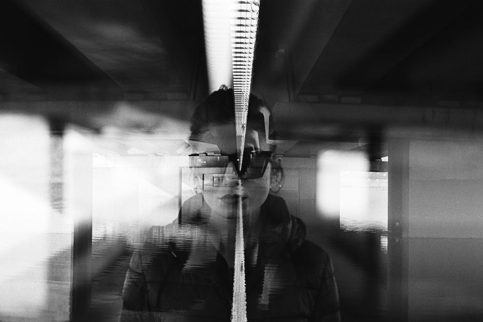 Artistic double exposure of a woman under a bridge with sunglasses reflecting a moody scene.