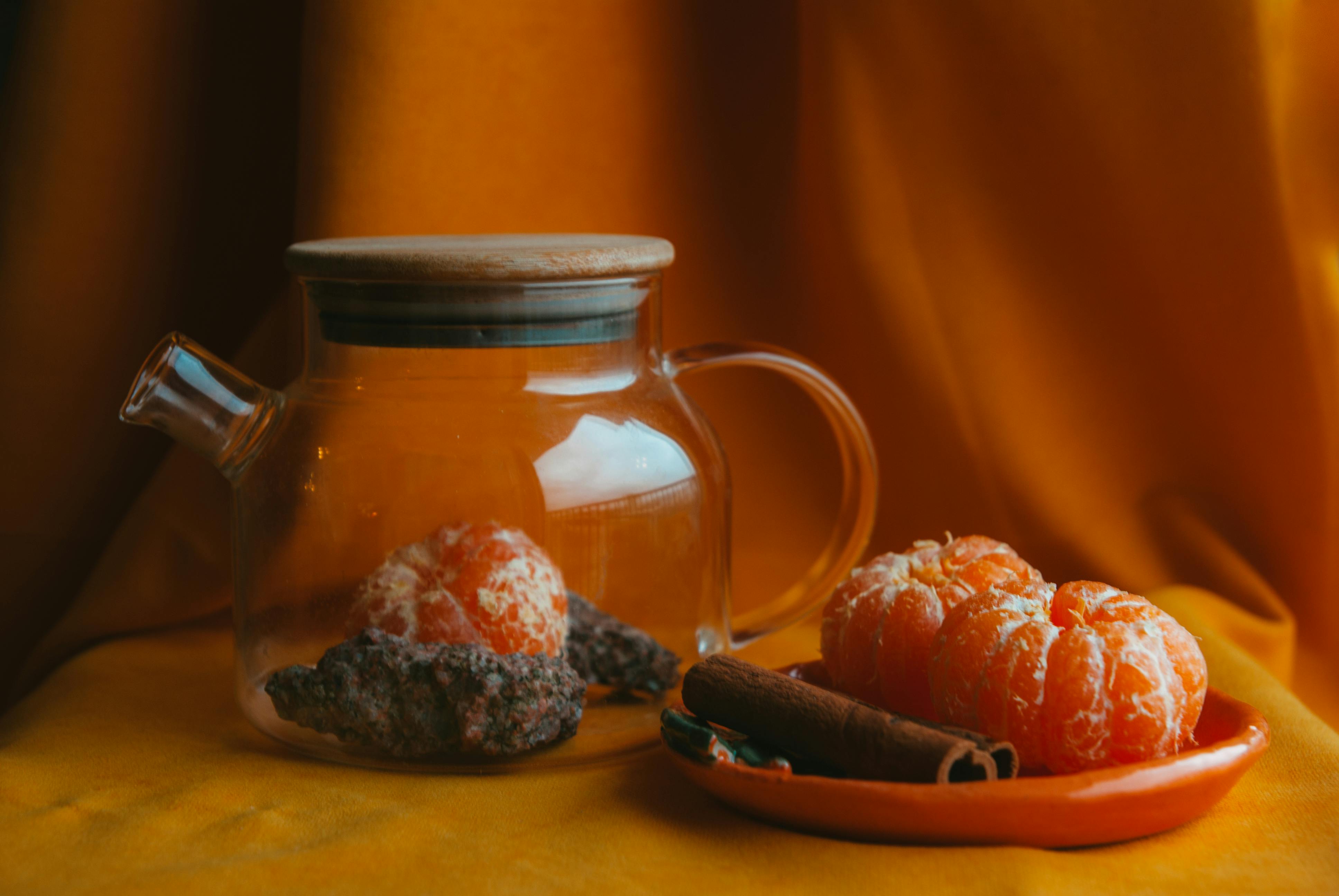 A warm still life featuring a glass teapot and tangerines against a cozy backdrop.
