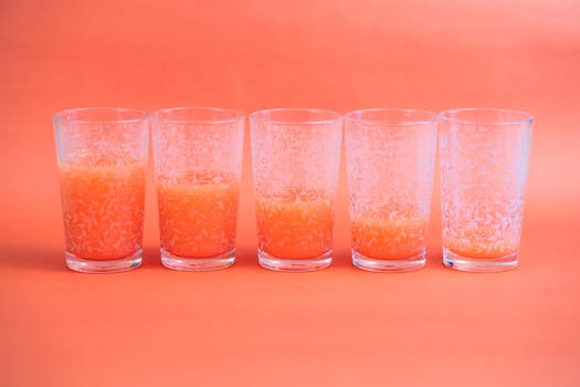 Five etched glasses with orange juice aligned on a pink background. Perfect for vibrant, modern themes.