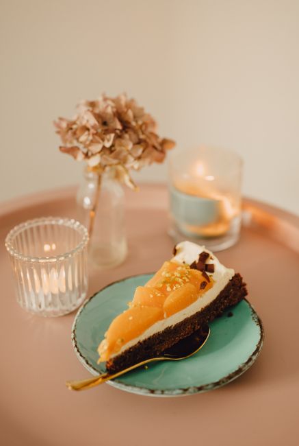 A stylish slice of peach tart on a teal plate with candlelight and floral decor. Perfect for a cozy dessert setting.