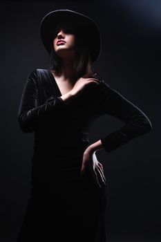 Artistic fashion portrait of a woman in a black velvet dress and hat, posing dramatically.