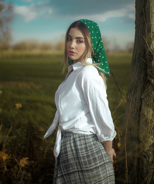 Free Portrait of a woman with a polka dot scarf in a vintage style, set against a rural field backdrop. Stock Photo