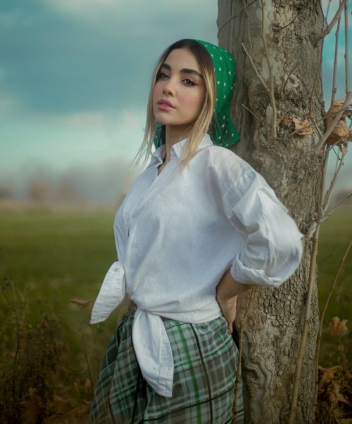 Free Woman in white shirt and green headscarf posing against a tree in a rural setting. Stock Photo