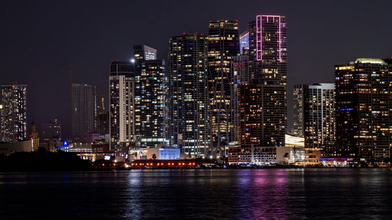Illuminated Miami skyline reflecting in dark water at night, a real aerial photo with no people in the frame, chosen because GTA 6's Vice City and its Florida-inspired state of Leonida are the backdrop of the launch trailer this story is about