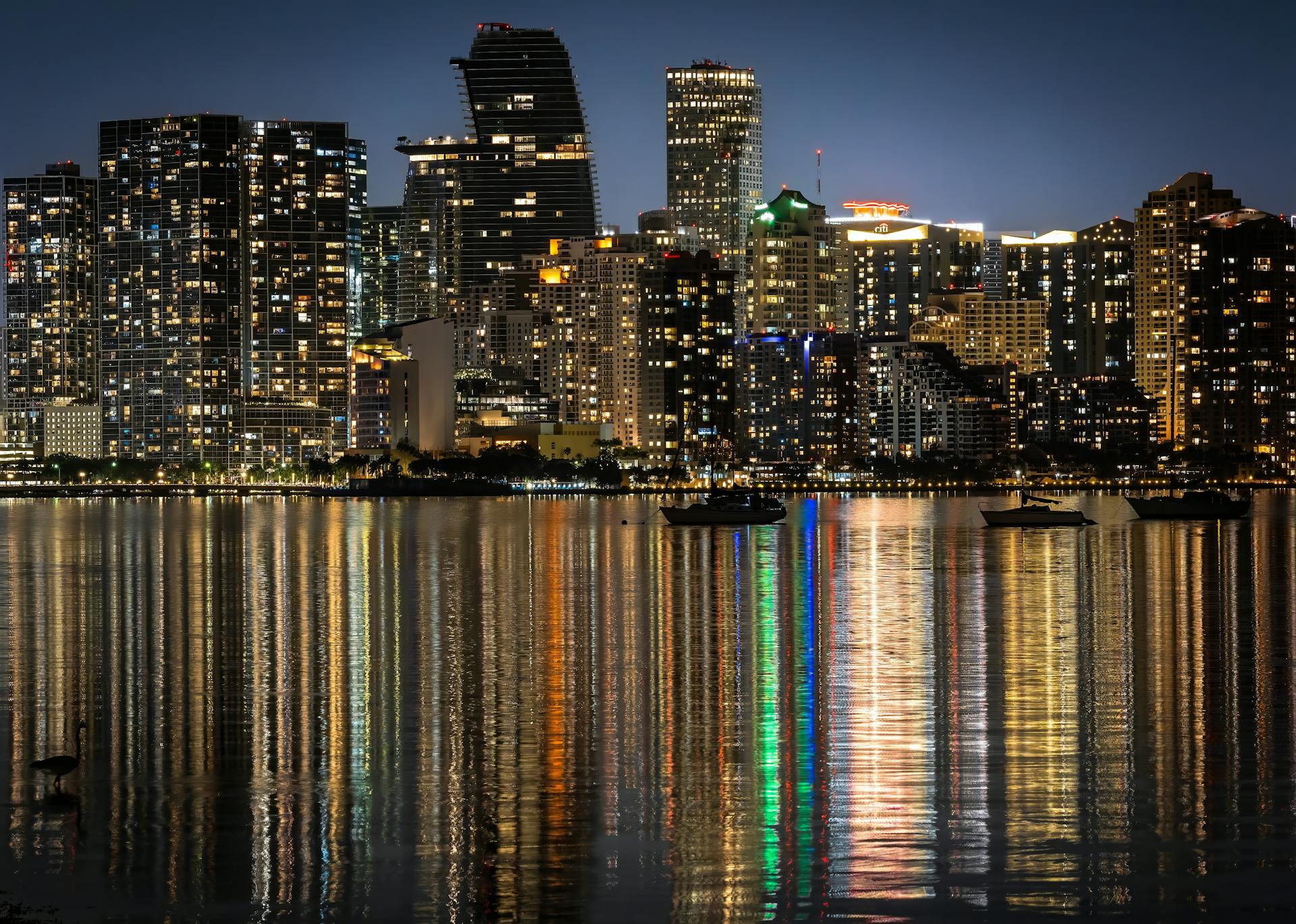 Captivating night view of Miami skyline with dazzling reflections on the water, showcasing city lights.