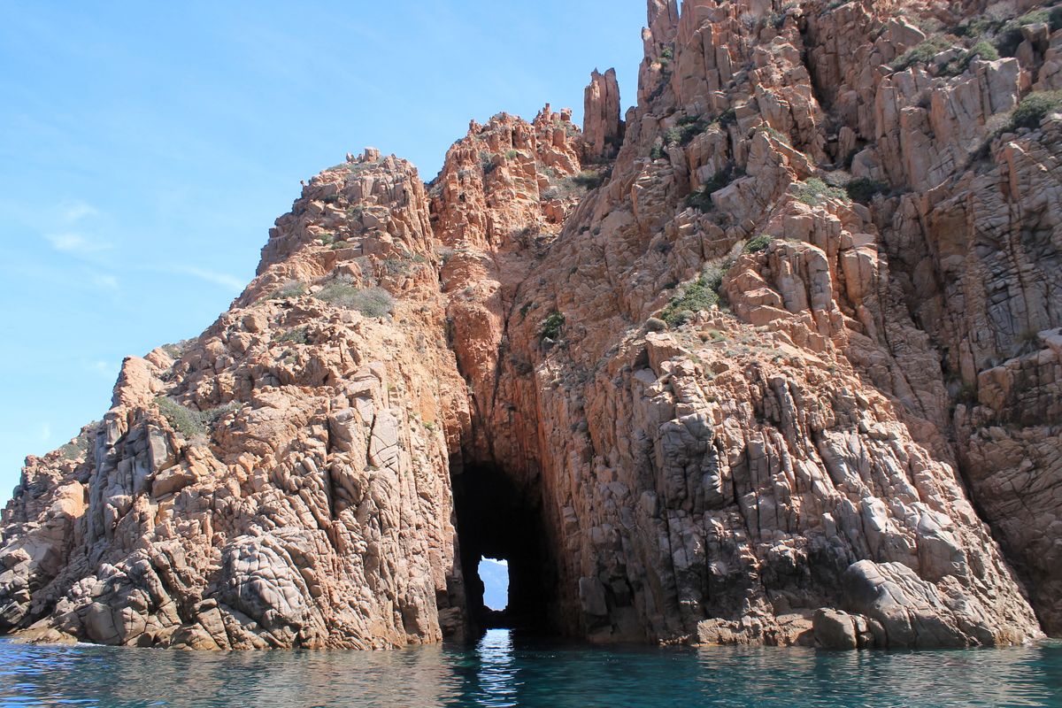 A red granite sea arch over turquoise water in the Piana calanques