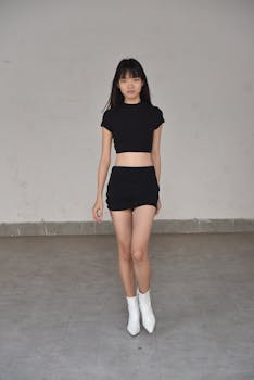 Stylish Asian woman in black outfit poses confidently against a minimal backdrop.