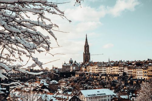 Free A scenic view of Bern, Switzerland with snow-covered rooftops and a historic cathedral under a winter sky. Stock Photo