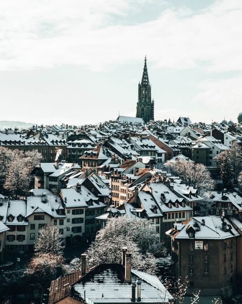 Free Charming snowy cityscape of rooftops and a tall spire during winter, showcasing urban beauty. Stock Photo