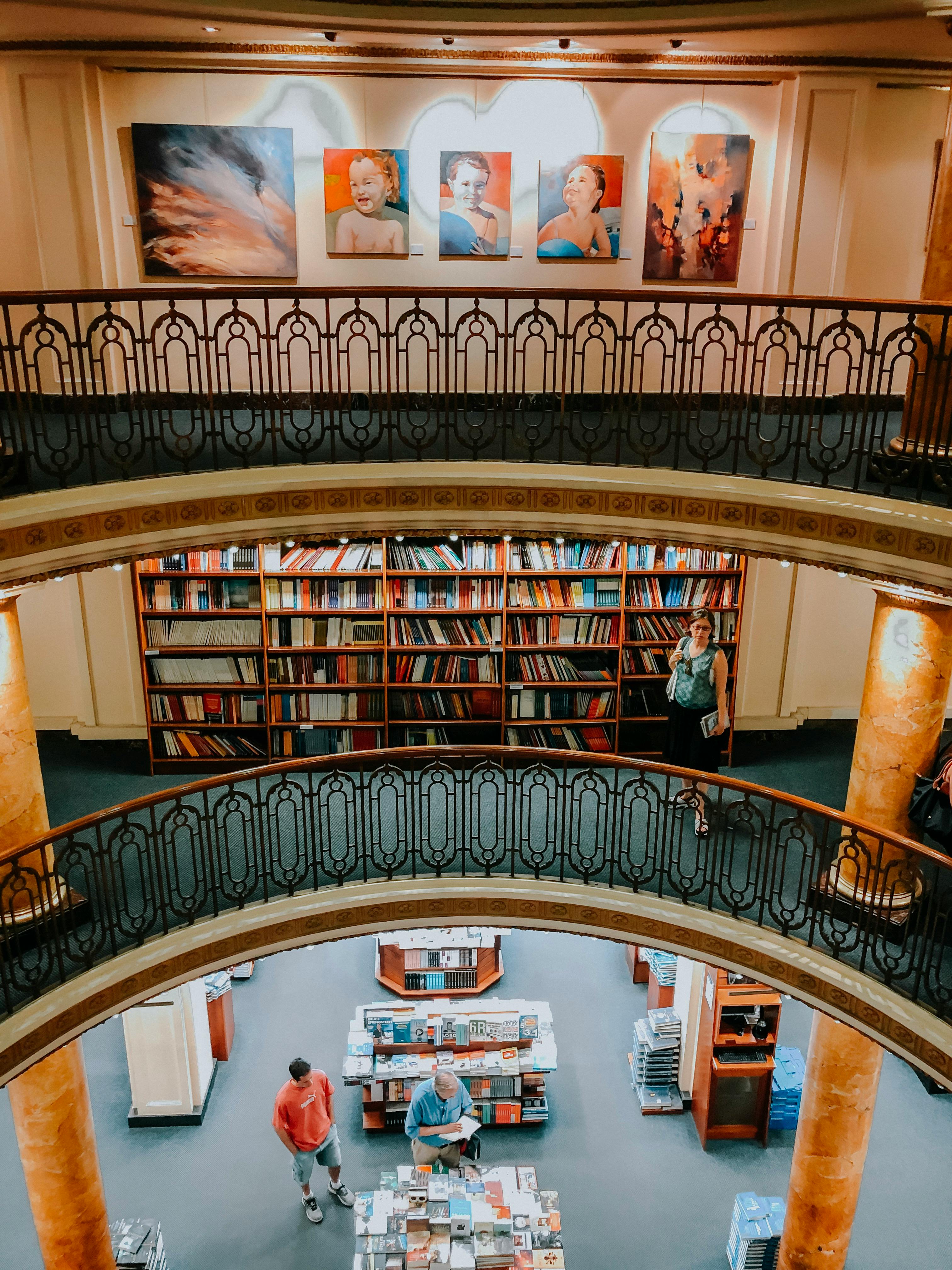 A vibrant library interior featuring multiple floors, artwork, and browsing visitors.