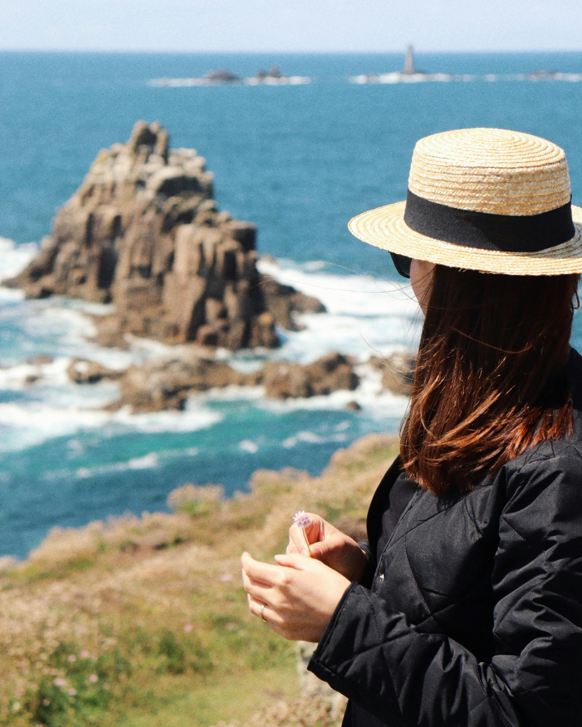 A woman in a straw hat and jacket stands at a scenic coastline in Elstree, England, Birleşik Krallık.