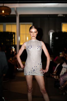 Model poses in a white mini dress on the runway during a fashion show.
