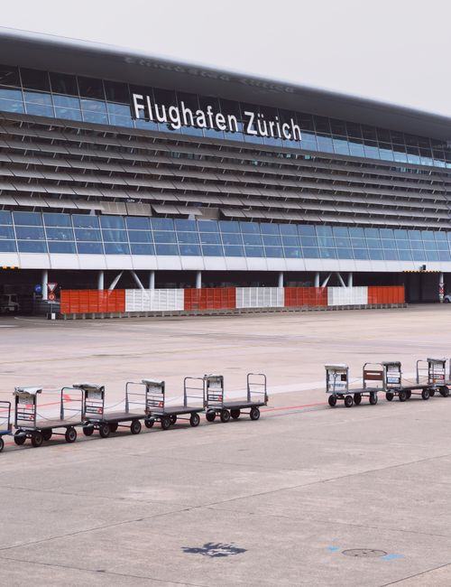 Free View of Zurich Airport terminal with aligned luggage carts on the tarmac. Stock Photo