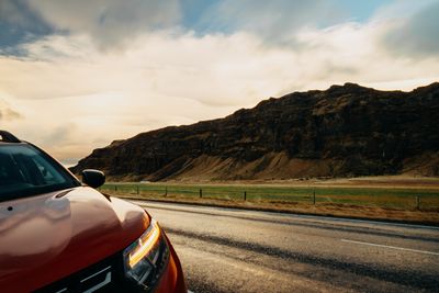 Red car on a rural road below a mountain ridge — photo by Matheus Bertelli on Pexels